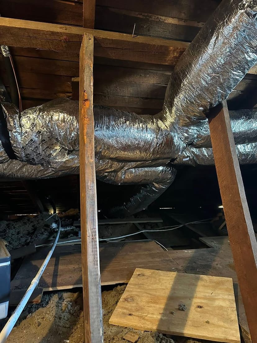 Insulated ductwork in an attic space with wooden beams and flooring visible.