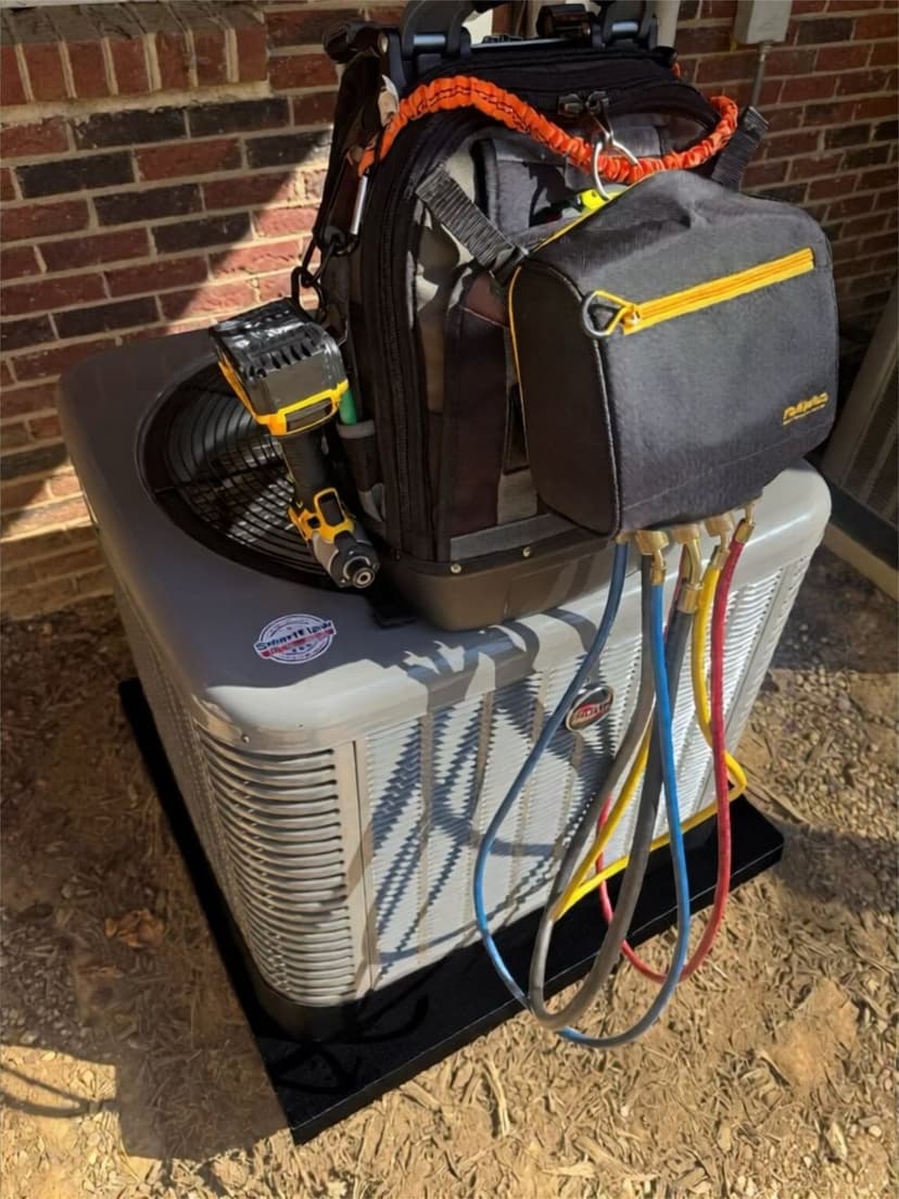 Backpack and tool bag on air conditioning unit with refrigerant lines attached.